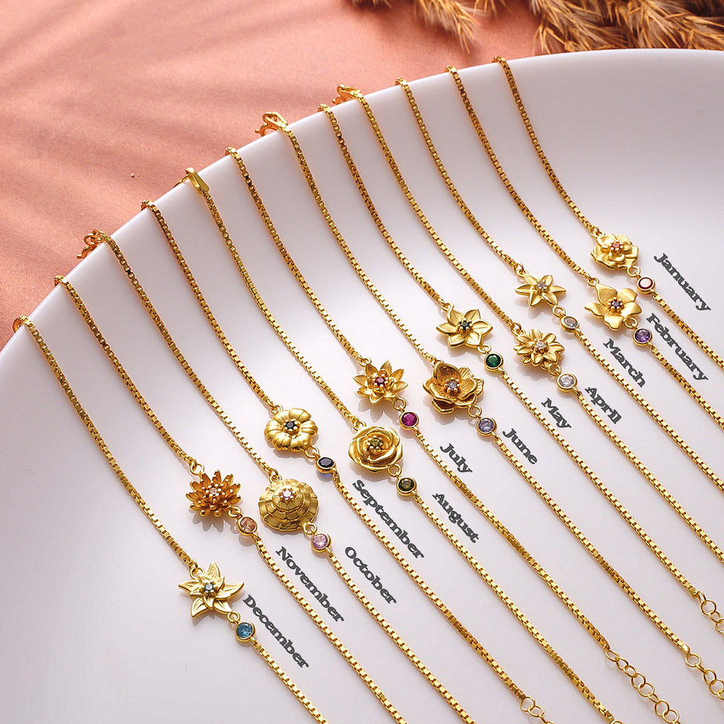 Gold necklaces with floral pendants on a white plate with month labels.