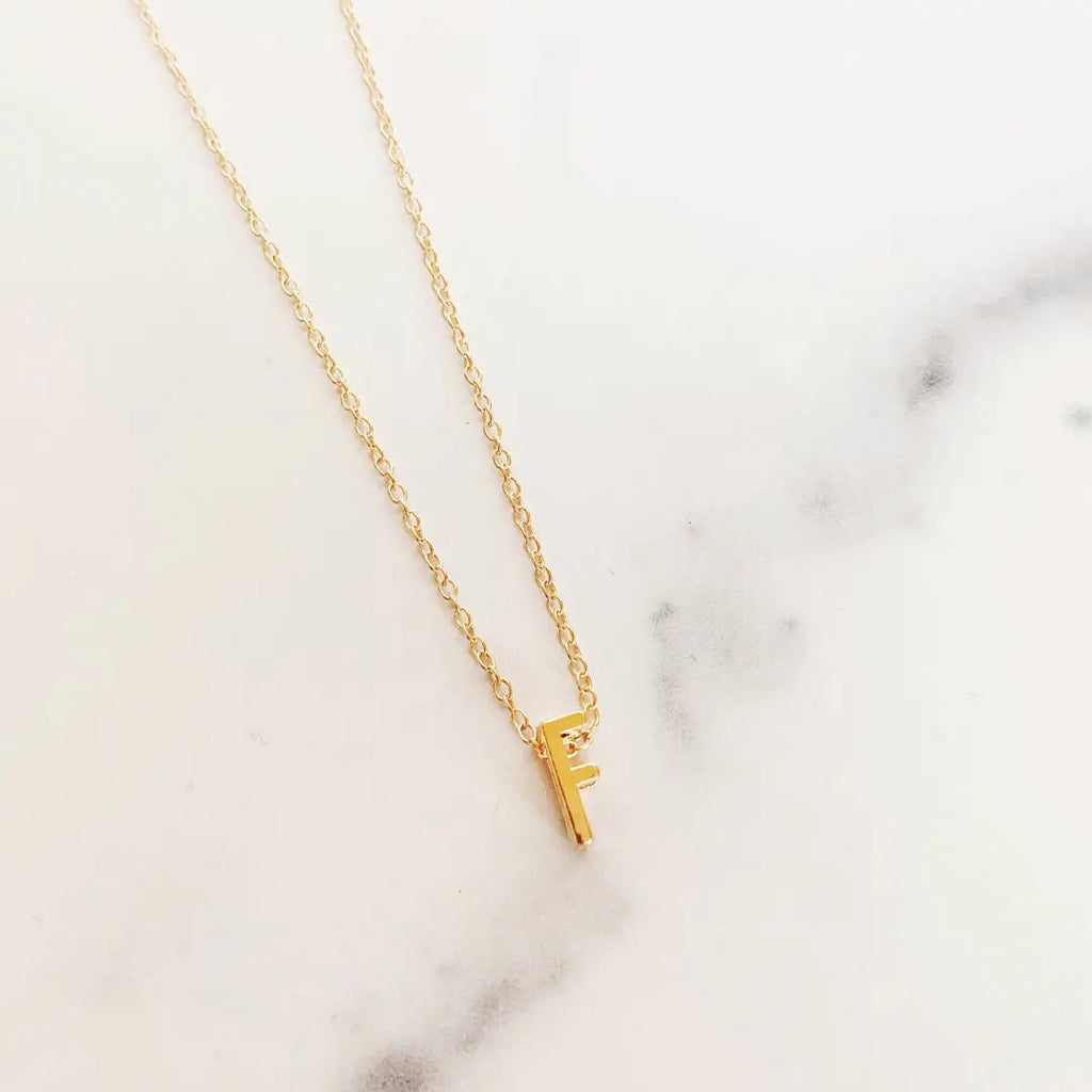 Gold necklace with a small letter 'F' pendant on a marble surface