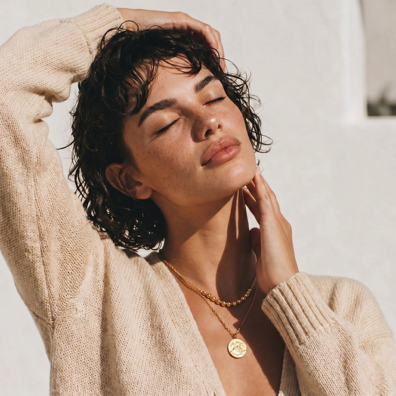 Woman wearing a beige sweater and gold necklace with a blurred background