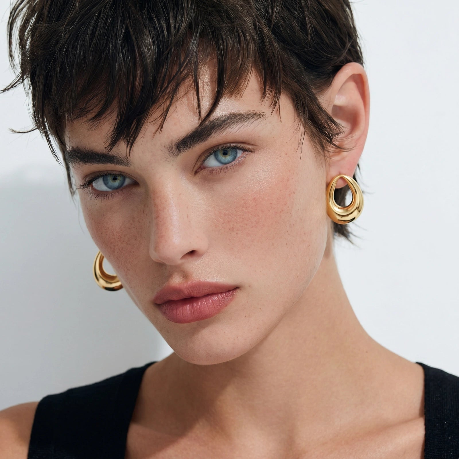 Close-up of a person wearing gold hoop earrings with a neutral background