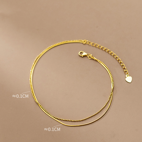 Gold anklet on a beige background with measurement text