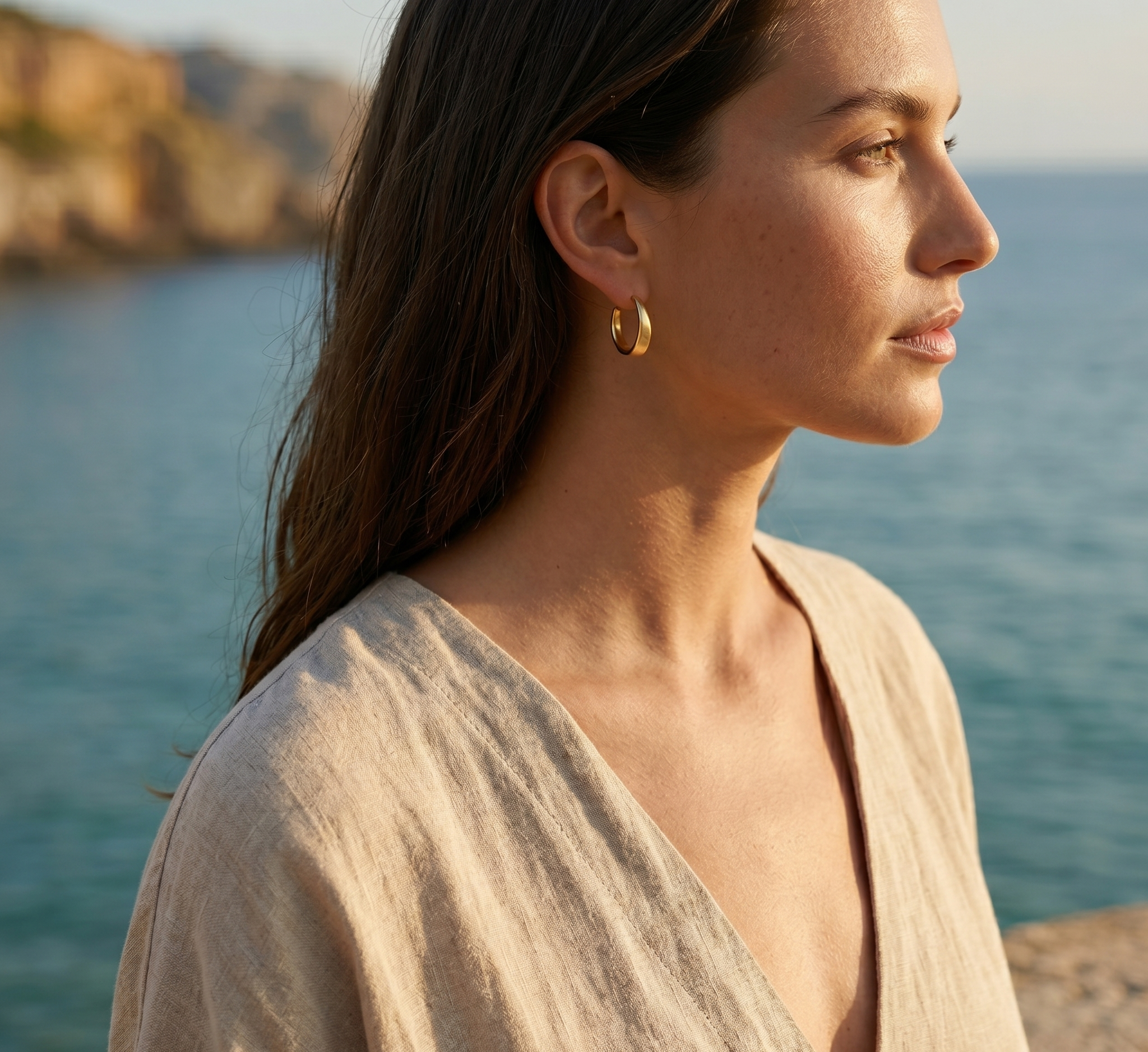 Woman wearing gold hoop earrings by a body of water