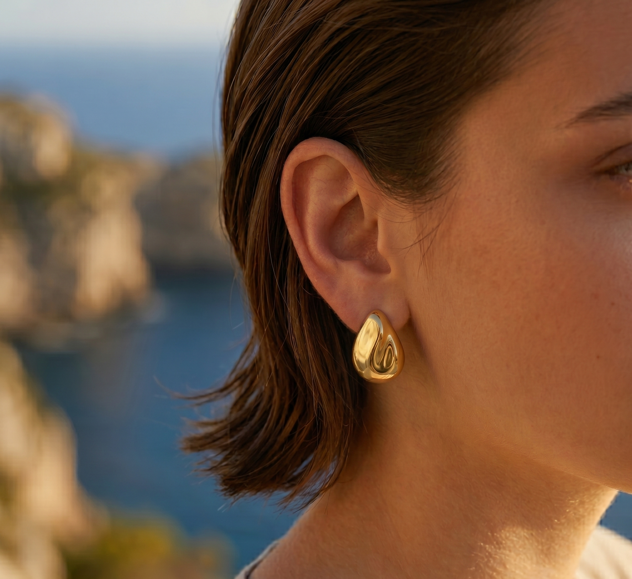 Close-up of a person wearing a gold earring with a scenic background