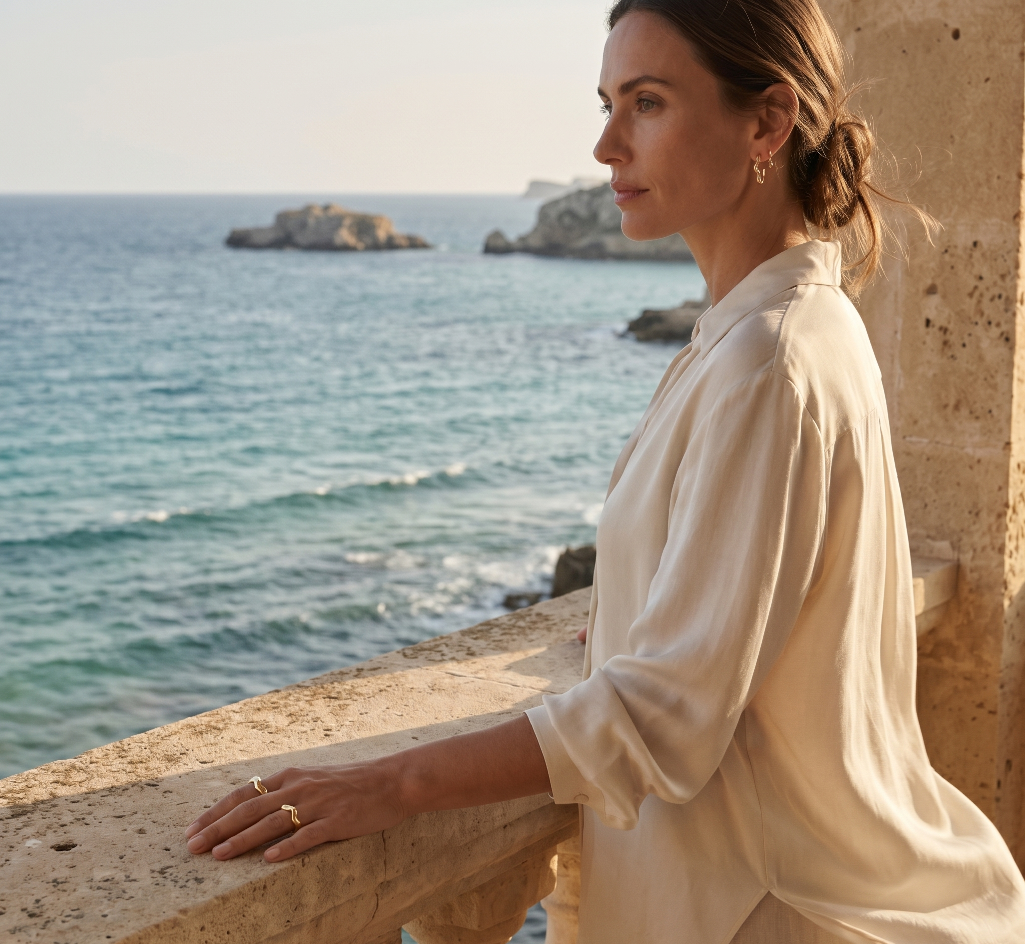 Woman in a white shirt standing on a balcony overlooking the ocean.