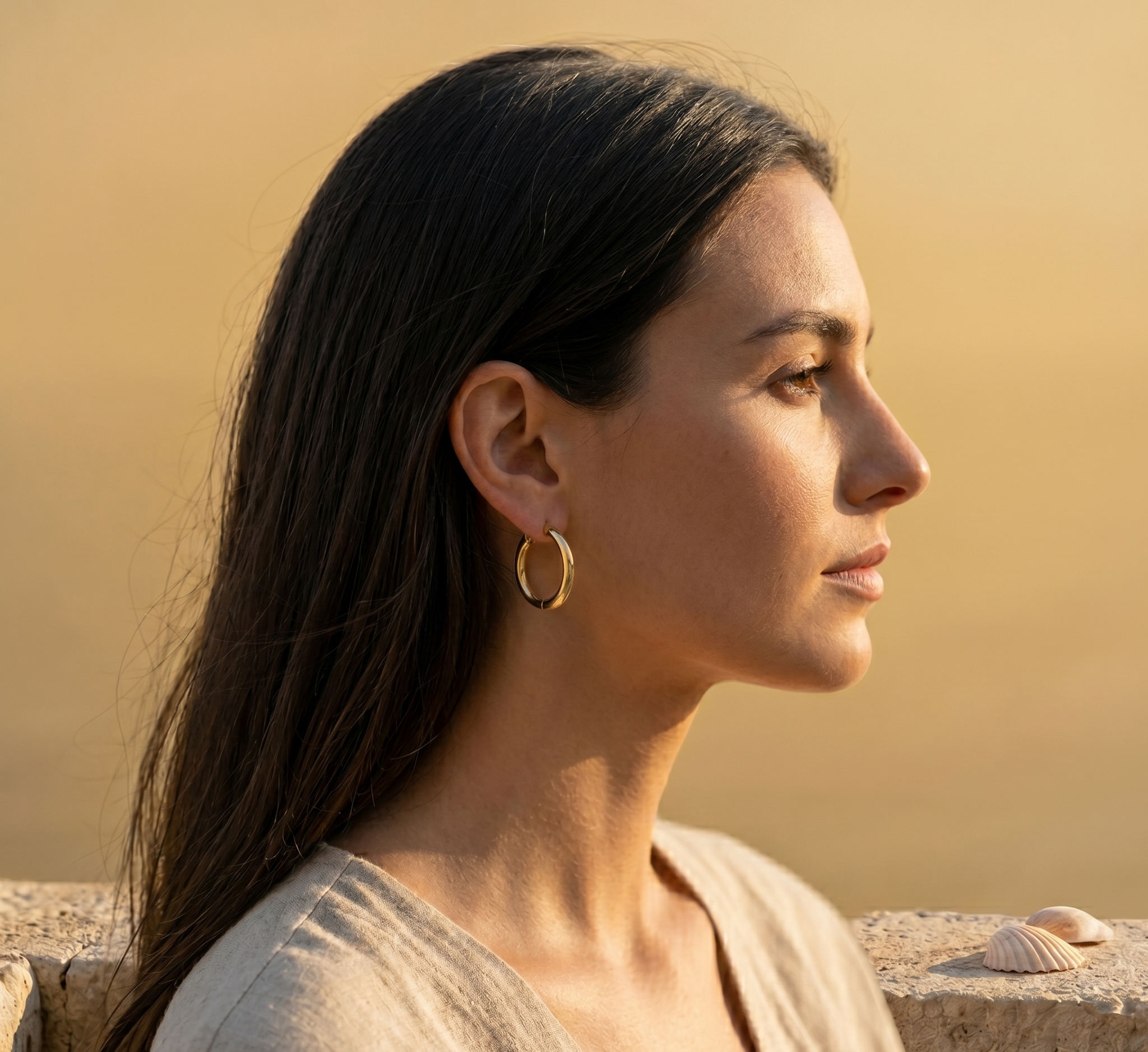 Woman with long dark hair and gold hoop earrings against a warm-toned background