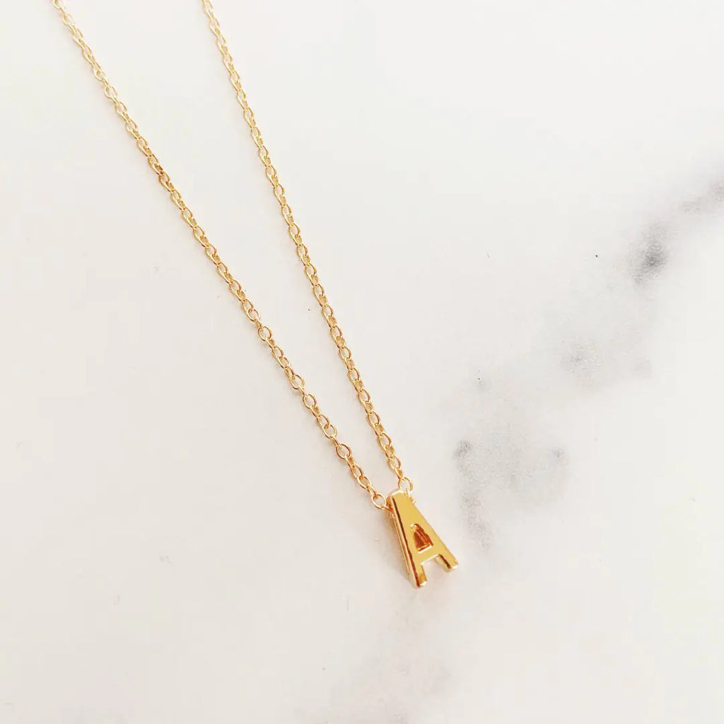Gold necklace with a small letter 'A' pendant on a marble background