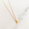 Gold necklace with a small letter 'A' pendant on a marble background