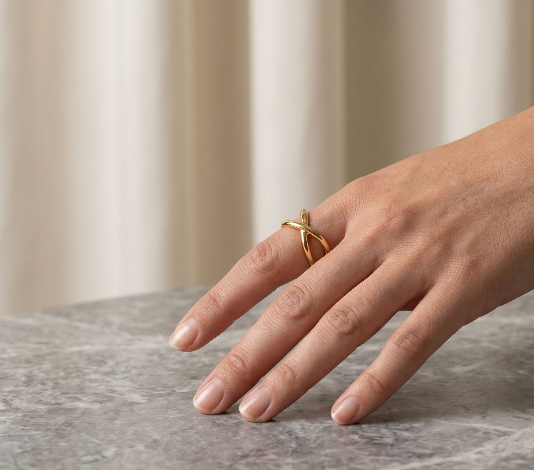 Hand wearing a gold ring and bracelet on a marble surface with a neutral background